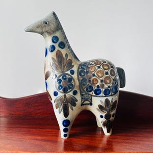 May include: A ceramic horse figurine with a white base and blue and brown floral patterns. The horse is standing on a wooden surface.