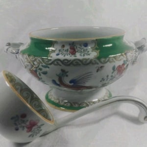 May include: A white ceramic soup tureen and ladle set. The tureen has a green rim and handles, with floral and bird designs. The ladle has a matching design. The set is likely vintage or antique.