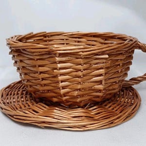 Puede incluir: Un juego de taza y platillo de mimbre tejido. La taza de té tiene un asa y se asienta sobre un platillo a juego. El juego está hecho de mimbre marrón claro y es adecuado para fines decorativos.