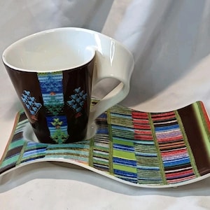 May include: A modern coffee cup and saucer set. The cup is brown with a patterned design and a white handle. The saucer has a matching pattern with a wavy design. The set is designed for serving coffee or tea.