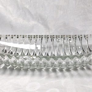 May include: A clear, elongated glass dish featuring a series of vertical, concave fluted channels along the interior walls and a textured, diamond-patterned exterior base. The vessel has a boat-like shape with tapered ends and a smooth, reflective surface.