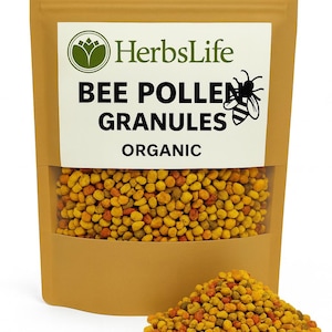 Op de afbeelding: Een bruine papieren zak met een doorzichtig venster met bijenpollenkorrels. De zak heeft een wit etiket met de tekst "HerbsLife BEE POLLEN GRANULES ORGANIC" en een bijengrafiek. Een kleine hoop korrels ligt ervoor.