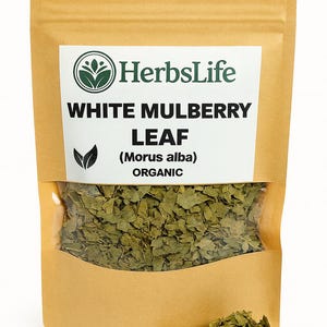 Könnte beinhalten: Ein brauner Papiersack mit einem transparenten Fenster, gefüllt mit getrockneten grünen weißen Maulbeerblättern. Der Beutel trägt das "HerbsLife"-Logo und den Text "WHITE MULBERRY LEAF (Morus alba) ORGANIC". Ein kleiner Blätterhaufen liegt davor.