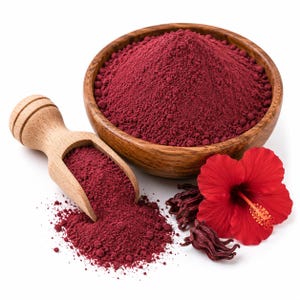 May include: A wooden bowl filled with deep red hibiscus powder, accompanied by a matching wooden scoop containing a portion of the powder. A vibrant red hibiscus flower and dried hibiscus calyces are placed next to the bowl on a white surface.