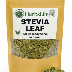 Puede incluir: Una bolsa de papel marrón con una ventana transparente que muestra hojas de stevia verdes secas. La bolsa tiene el texto "HerbsLife STEVIA LEAF (Stevia rebaudiana) ORGANIC" en blanco y verde. Un pequeño montón de hojas de stevia está delante de la bolsa.
