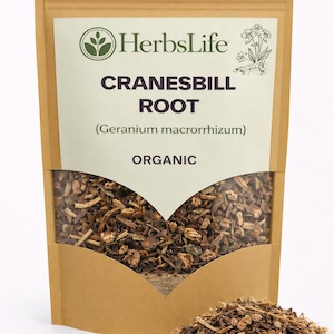 May include: A brown paper bag with a white label displaying the text "HerbsLife CRANESBILL ROOT (Geranium macrorrhizum) ORGANIC." The bag contains dried root pieces, with a small pile of the root in front.