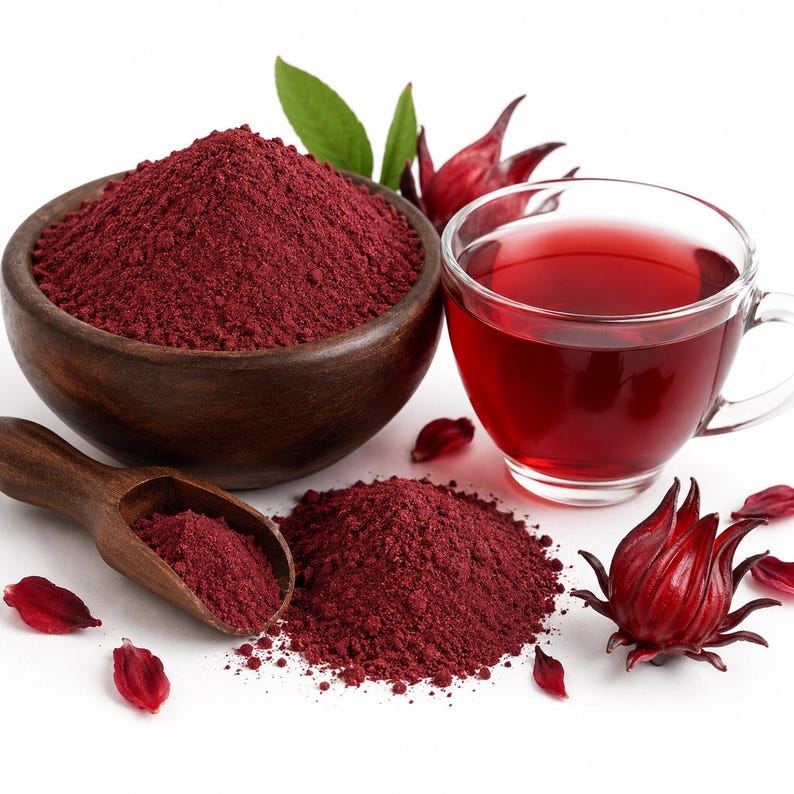 May include: A dark wooden bowl filled with deep red hibiscus powder, a matching wooden scoop containing more powder, a clear glass cup of red hibiscus tea, and several fresh red hibiscus calyxes with green leaves on a white surface.