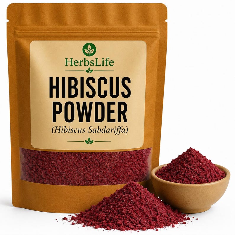 May include: A brown stand-up pouch labelled HerbsLife Hibiscus Powder (Hibiscus Sabdariffa) with a clear window showing deep red powder. Next to the pouch is a small tan bowl filled with the same vibrant red hibiscus powder, with a pile in front.