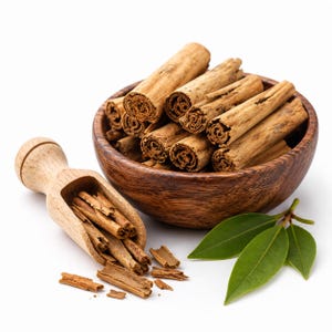 May include: A dark wooden bowl filled with light brown cinnamon sticks, accompanied by a matching wooden scoop containing smaller cinnamon pieces and fragments, alongside three fresh, smooth, pointed green leaves on a plain white background.