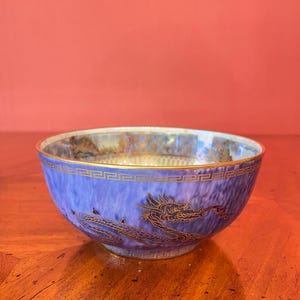 May include: A blue ceramic bowl with a gold dragon design. The bowl has a gold rim and a textured blue surface. The dragon is depicted in gold, adding a touch of elegance to the piece.