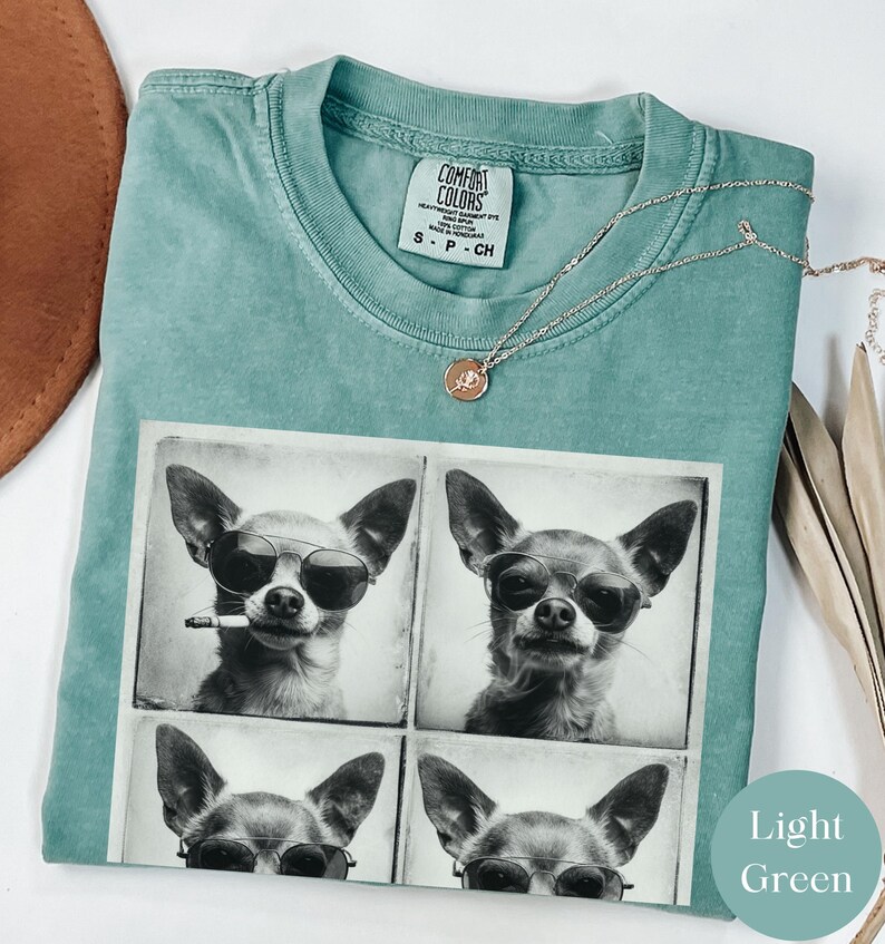 Pu&ograve; includere: T-shirt Comfort Colors verde chiaro con un collage fotografico in bianco e nero di un chihuahua con occhiali da sole, uno con una sigaretta. &Egrave; visibile anche una collana d'argento con un piccolo ciondolo.