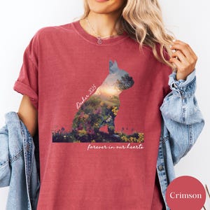 May include: Crimson-colored t-shirt featuring a silhouette of a dog filled with a landscape design. The text "Dasher 2025" is above the dog, and "forever in our hearts" is below. The shirt has rolled-up sleeves.