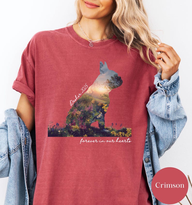 May include: Crimson-colored t-shirt featuring a silhouette of a dog filled with a landscape design. The text "Dasher 2025" is above the dog, and "forever in our hearts" is below. The shirt has rolled-up sleeves.