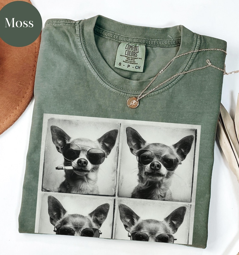 Pu&ograve; includere: Una maglietta Comfort Colors verde muschio con un'immagine a quattro pannelli di un chihuahua con occhiali da sole. Un chihuahua ha una sigaretta in bocca. Una collana d'oro con un piccolo ciondolo &egrave; drappeggiata sulla maglietta.