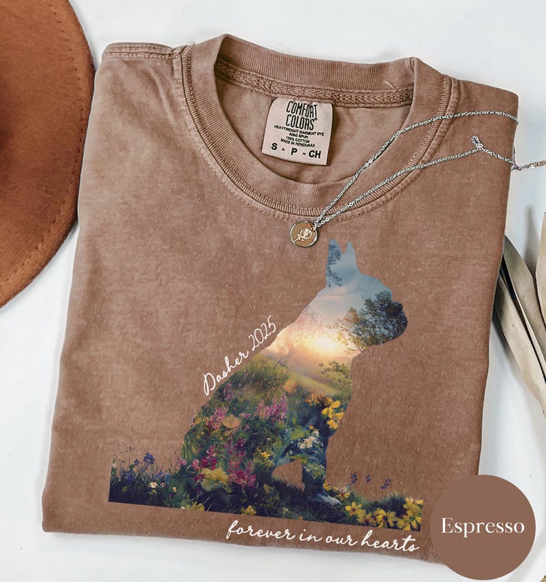May include: Espresso-colored t-shirt with a dog silhouette filled with a landscape of flowers and a sunset. The shirt has the text "Dasher 2025" and "forever in our hearts". A silver necklace with a pendant is on the shirt.