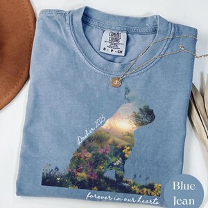 May include: A light blue Comfort Colors t-shirt featuring a dog silhouette filled with a floral landscape and the text "Dasher 2025" and "forever in our hearts". A gold necklace with a pendant rests on the shirt.