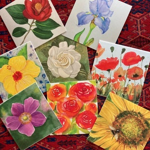 May include: Set of ten watercolor paintings of various flowers, including a camellia, iris, gardenia, poppy, anemone, rose, and sunflower. Each painting is on a white card with a green border.