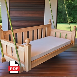May include: A wooden porch swing with a light-colored finish. The swing features a slatted back and sides, a white cushion, and decorative ball finials on the posts. It hangs from green and yellow rope.