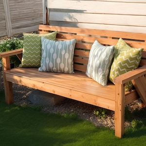 May include: A wooden outdoor bench with four decorative pillows. The bench is made of light brown wood and has a slatted back. The pillows are green and white with various patterns, including zigzags and oval shapes.
