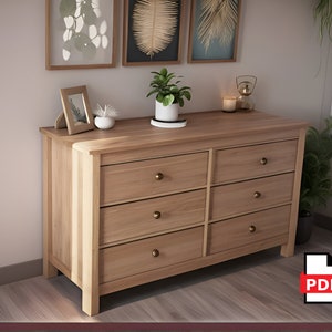May include: A light wood dresser with six drawers and brass knobs. The dresser is in a room with a light wood floor and a white wall. There are framed pictures and plants on the wall above the dresser.