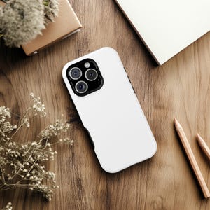 May include: A white phone case with a black camera lens cutout. The case is on a wooden surface.