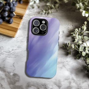 May include: A smartphone case with a watercolor design in shades of purple and blue. The case has a glossy finish and a camera cutout. The case is lying on a marble surface.