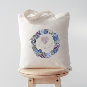 May include: A white canvas tote bag featuring a wreath of yarn balls and knitting needles. The wreath has a pink heart in the centre with the text "Knitting Fun".