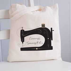 May include: A white canvas tote bag with a black silhouette of a sewing machine and the text "Granny's Sewing Bits".