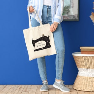 May include: A beige canvas tote bag with black handles. The bag features a black silhouette of a sewing machine with the text "Lucy's Sewing Bits" printed on it.