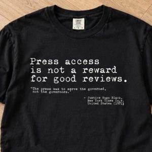 May include: A black crew neck t-shirt featuring white typewriter-style text that reads: Press access is not a reward for good reviews. The press was to serve the governed, not the governors. - Justice Hugo Black, New York Times Co. v. United States (1971).