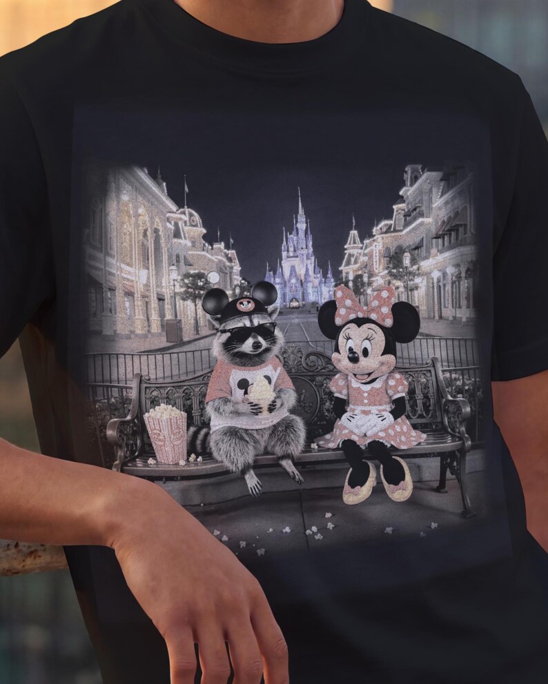 Może przedstawiać: Czarny t-shirt z fantazyjną grafiką szopa pracza i Myszki Minnie siedzących na ławce przed zamkiem. Szop nosi okulary przeciwsłoneczne i r&oacute;żową koszulkę, a Myszka Minnie ma na sobie r&oacute;żową sukienkę w kropki. W pobliżu znajduje się pudełko popcornu.
