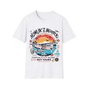 Pode incluir: Camiseta branca com um design gráfico vintage que apresenta um avião voando sobre uma ilha tropical. O design inclui o texto "Howlin' Murdocks", "Tropical Island Sky Tours" e "Est. 83".