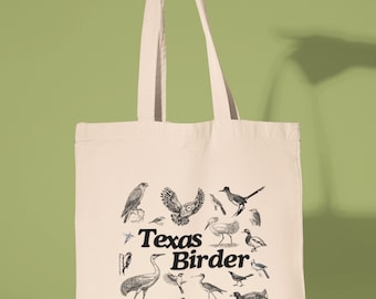 May include: Cream-colored tote bag featuring a collection of detailed bird illustrations in black and white. The text "Texas Birder" is printed in a bold, black font. The bag is held by a person against a green background.