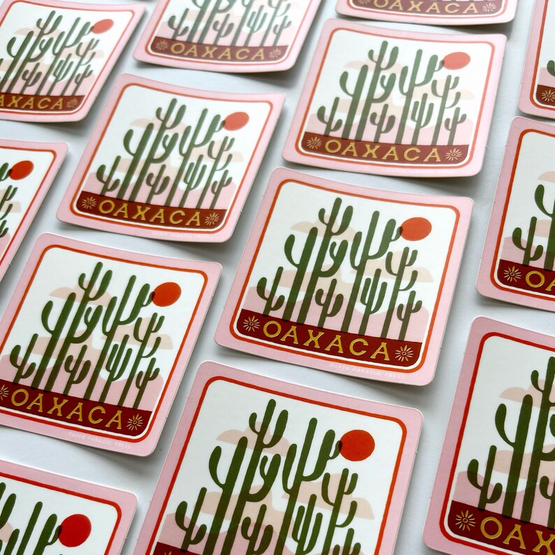 May include: A set of pink and white stickers featuring a graphic of a cactus landscape and the word "Oaxaca" in gold lettering. The stickers are square shaped and have rounded corners.