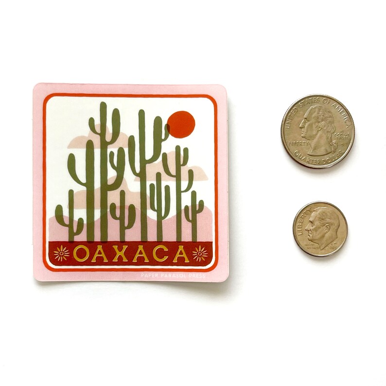 May include: Pink sticker featuring a graphic of a desert landscape with cacti and a red sun. The text "OAXACA" is in gold letters with a star on either side. The sticker is from Paper Parasol Press.