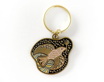 May include: Gold-tone key chain with a black and gold enamel charm featuring a stylized bird with pink accents.