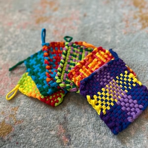 May include: A set of six colorful woven pot holders, each with a different pattern. The pot holders are made with a variety of colors, including red, orange, yellow, green, blue, and purple.