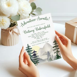 Könnte beinhalten: Eine Babyparty-Einladung mit dem Text "Adventure Awaits!" in grüner Schrift. Die Einladung zeigt ein Aquarelldesign von Bergen, Bäumen und einer untergehenden Sonne. Die Einladung enthält den Namen "Britney Bakersfield" und Veranstaltungsdetails.