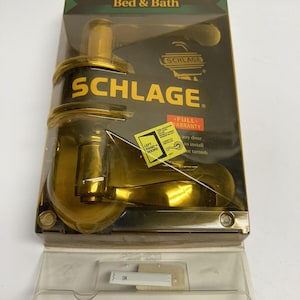 May include: A gold Schlage door handle in a plastic package. The package has the text "Bed & Bath" and "FULL WARRANTY" on it. The door handle is for left-hand doors.