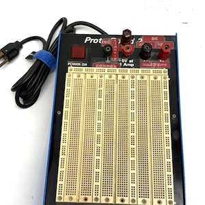 May include: A black and blue Protoboard 2 with a power cord and breadboards. The board has red and black terminals, a power indicator, and the text "+5V at 1 Amp". The bottom of the board reads "GLOBAL SPECIALTIES CORPORATION, NEW HAVEN, CONNECTICUT 06509".