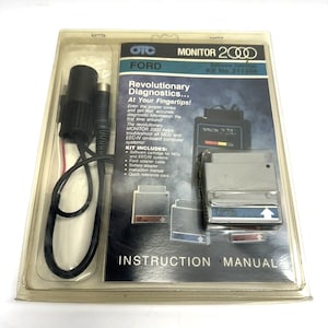 May include: A silver and black car diagnostic tool with a black cable and a cigarette lighter adapter. The tool is labeled "MONITOR 2000" and "FORD". The packaging includes an instruction manual and a quick reference card.  The text on the packaging reads "Revolutionary Diagnostics... At Your Fingertips!" and "Kit No. 211356".