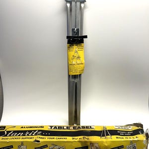 May include: A silver aluminum Stanrite table easel in a yellow and black box. The box reads "Stanrite... Table Easel... Rigid Locked Support - Carry Your Canvas... Wet or Dry..." and "Instantly Opens and Closes. Made in U.S.A."