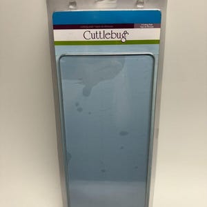May include: A package containing two blue cutting mats for use with a Cufflebug die-cutting machine. The package is labeled "Cufflebug Cutting Pads - Tapis de découpage - 2 Cutting Pads - Tapis de Découpage".