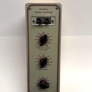 May include: A vintage Heathkit Decade Condenser, model FCN-77, with a light gray face and red trim. It features three black knobs with white markings for micro-micro farads and micro farads. The device has a series of dials and a connector.