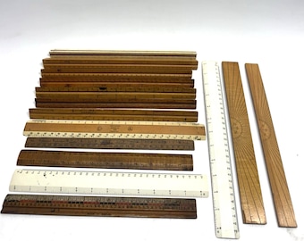 May include: A collection of vintage wooden and plastic rulers in various shades of brown and white. The rulers are of different lengths, some with etched markings and designs. A few rulers have a sunburst design.
