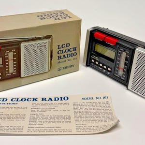 May include: An Equity brand LCD clock radio, model number 161, featuring a black and silver rectangular body with a digital display, analog radio tuner, and speaker grille. The item is shown with its original cardboard box and printed instructions.