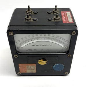 May include: A black Esterline Electronics Corporation milliammeter with a gauge displaying numbers from 0 to 1500. The meter has four terminals on top and a label that reads "MILLIAMPERES D.C."