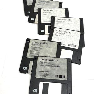 May include: A collection of black 3.5-inch floppy disks with white labels. The labels read "Lotus Ami Pro Release 3.0" and "ATM Program Disk". The disks are arranged on a white surface, showcasing a retro computer software theme.