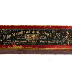 May include: A vintage rectangular box with a red and black label. The label reads "THE GENUINE AND ORIGINAL IRWIN BITS" and "THE IRWIN AUGER BIT COMPANY". The box is worn, with visible signs of age and use.