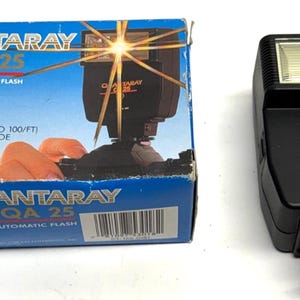 May include: A Quantaray QA 25 computerized automatic flash unit and its original box. The black flash has a rectangular head and a control panel. The box is blue with white and red text, including "2-RANGE AUTOMATIC" and "GUIDE NUMBER 60".